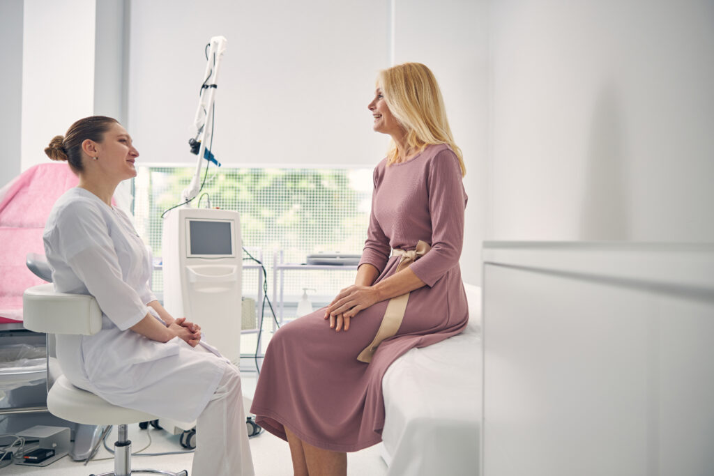 Pleased smiling female gynecologist sitting while listening to her patient 
