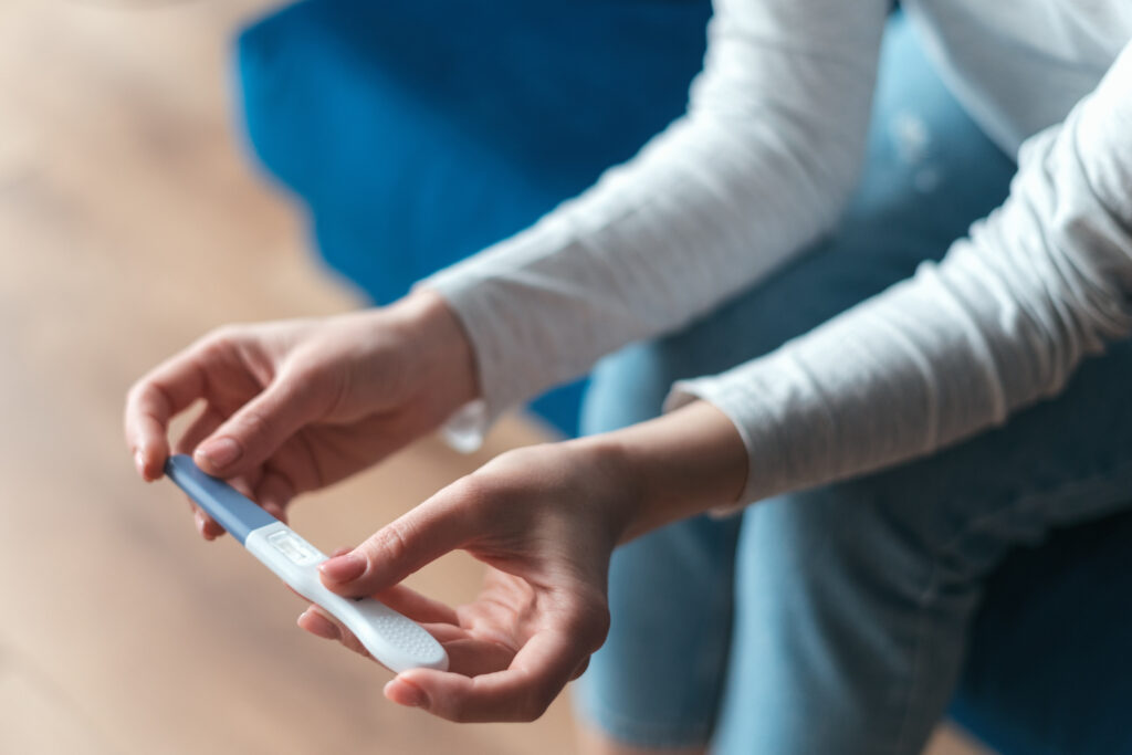 Cropped view of woman hands with domestic pregnancy test being at home. Process of waiting for test results when sitting on sofa. Motherhood concept