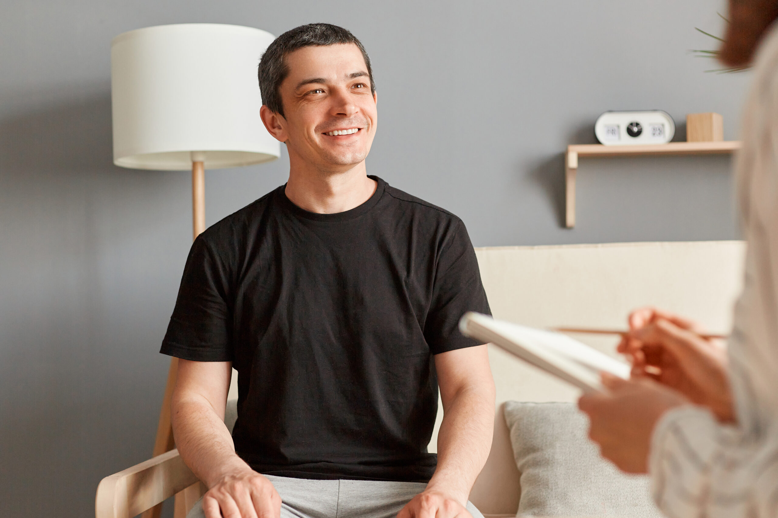 Inspired handsome young man in black T-shirt sitting on couch at counselor office, sharing feelings, thoughts with therapist woman, enjoying therapy session.