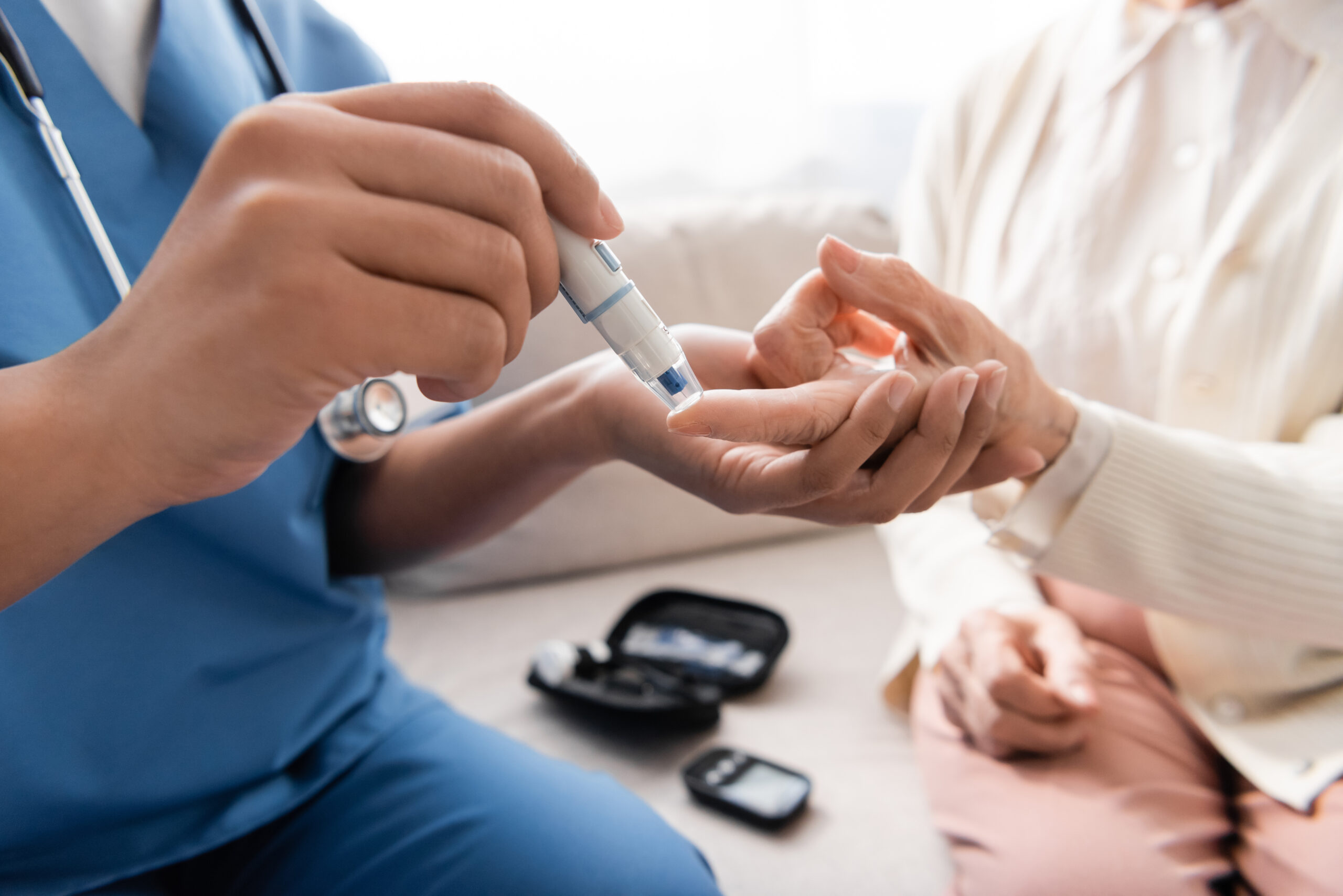 cropped view of multiracial nurse taking blood sample of senior woman with lancet pen,stock image